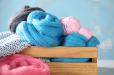 Masanın üzerindeki ahşap sandıkta yumuşak yün ve örgü ipliği açık mavi arka planda bulanık ışıklar, yakın plan