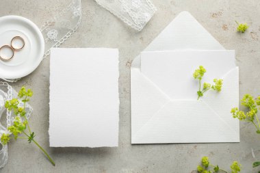 Düğün davetiyeleri, altın yüzükler, çiçekler ve zarf gri desenli masa, düz uzanış