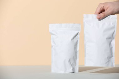 Gri masadaki boş fermuarlı stand-up torbalarını bej arka planda tutan kadın, yakın plan. Metin için boşluk