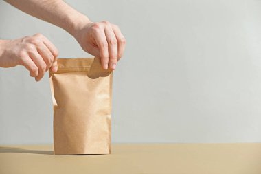 Açık gri arkaplanlı, yakın plan, bej masanın üzerinde boş bir fermuar stand-up çantası tutan kadın. Metin için boşluk