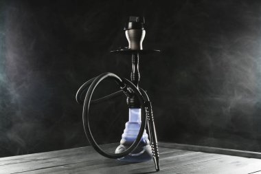 Siyah arka planda duman olan ahşap masada nargile.