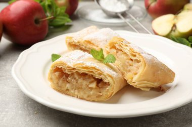 Lezzetli elmalı turta parçaları pudra şekeri, nane ve meyveler gri masada, yakın plan.