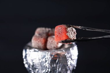 Koyu arkaplanda maşayla yanan kömür küpü, yakın plan