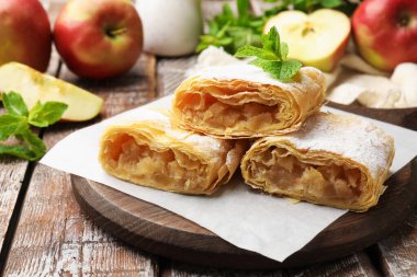 Lezzetli elmalı turta parçaları pudra şekeri, nane ve ahşap masada meyveler, yakın plan.