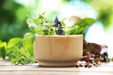 Tahta masanın üzerinde farklı taze otlar bulunan havan topu bulanık yeşil arka planda, yakın plan