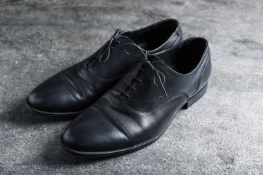 Gri yüzeyde bir çift siyah deri ayakkabı, yakın plan.