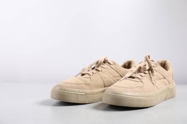 Açık gri yüzeyde bir çift bej spor ayakkabı, yakın plan. Metin için boşluk