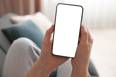 Evdeki koltukta modern akıllı telefon kullanan bir kadın.