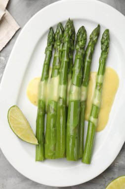 Sos ve limonla servis edilen lezzetli pişmiş kuşkonmaz. Gri desenli masa, üst manzara.