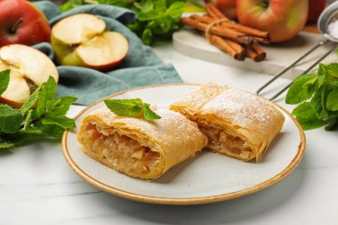 Lezzetli elmalı turta parçaları pudra şekeri, nane, meyve ve tarçın beyaz mermer masada, yakın plan.