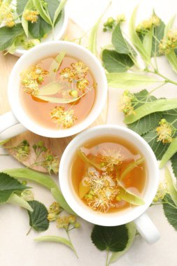 Taze ıhlamur çayı fincanda ve çiçekler beyaz masada, düz yerde.