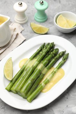 Sos ve limonla servis edilen lezzetli pişmiş kuşkonmaz. Gri desenli masa, yakın plan.