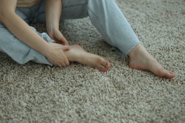 Woman suffering from foot pain on floor at home, closeup
