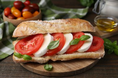 Mozarella peynirli, domatesli ve ahşap masadaki fesleğenli lezzetli sandviç.