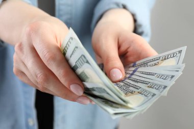Açık gri arka planda dolar banknotları sayan kadın, yakın plan