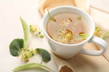 Fincanda taze ıhlamur çayı ve beyaz masada çiçekler, yakın plan.