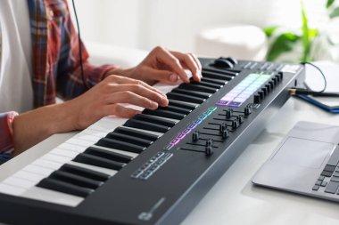 Beyaz masada MIDI klavyesiyle çalışan adam, yakın plan.