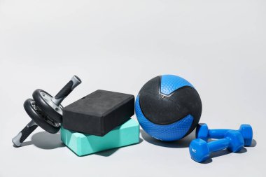 Açık gri arka planda sağlık topu, dambıl, kas çarkı ve köpük blokları