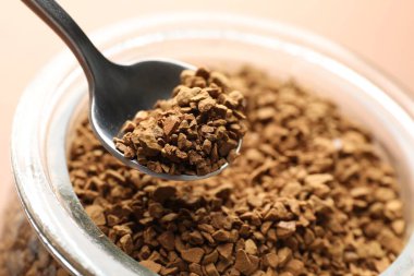 Kavanozdan bej arka planda kaşıkla granülatif hazır kahve almak, yakın plan.