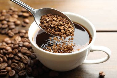 Tahta masadaki sıcak içeceğe hazır kahve koymak, yakın plan.