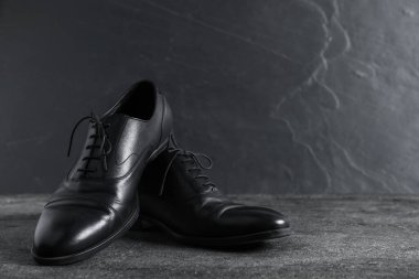 Gri yüzeyde bir çift siyah deri ayakkabı, yakın plan. Metin için boşluk