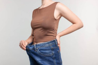 Açık gri arka planda kilo verdikten sonra eski kot giyen kadın, yakın plan.