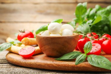 Lezzetli mozzarella peyniri topları, domatesler, fesleğen ve grissini ahşap masada, yakın plan.