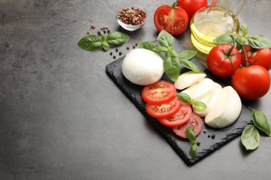 Lezzetli mozzarella peyniri, domates, fesleğen ve baharatlar gri masada. Metin için boşluk