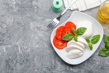 Lezzetli mozzarella peyniri, domates, fesleğen ve baharatlar gri masada. Metin için boşluk