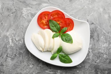 Lezzetli mozzarella peyniri, domates ve fesleğen gri masada.