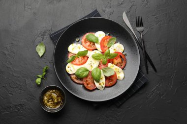 Peynirli Caprese salatası, domates, fesleğen ve baharatlar siyah masada, düz yerde.