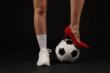 Arka planda futbol topu olan yüksek topuklu ayakkabılı ve spor ayakkabılı bir kadın.