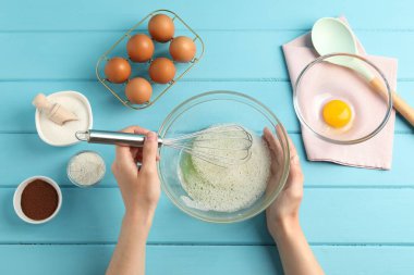 Bir kadın açık mavi ahşap masada kasede yumurta akı çırpıyor.