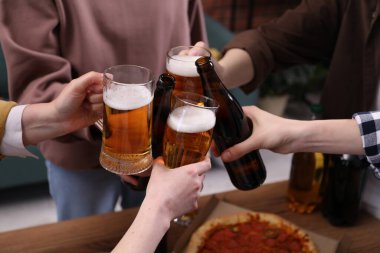 Arkadaşlar masada bira bardaklarını tokuşturur, yakın plan
