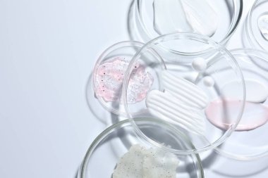 Petri kabında farklı kozmetik ürünleri, beyaz arka planda, düz yerde. Metin için boşluk