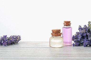 Beyaz arka plana karşı ahşap masa üzerinde doğal yağ ve lavanta çiçekleri