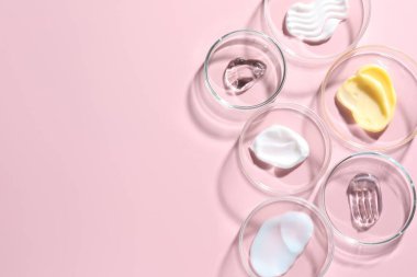 Petri kaplarında pembe arka planda farklı kozmetik ürünleri var. Metin için boşluk