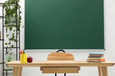 Farklı okul kırtasiyesi ve kırmızı elma, kapalı alanda tahtaya yakın ahşap masada.