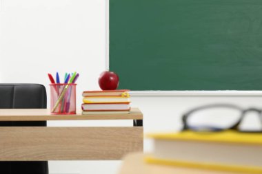 Farklı okul kırtasiyesi ve kırmızı elma, kapalı alanda tahtaya yakın ahşap masada.