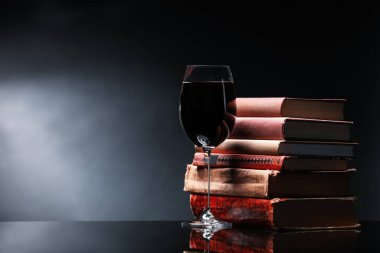 Bardakta lezzetli şarap ve karanlık arka planda ayna masasında yığınla kitap. Metin için boşluk