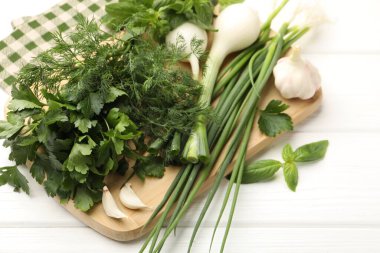 Farklı taze otlar, yeşil soğanlar ve beyaz ahşap masada sarımsak, yakın plan.