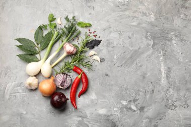 Farklı taze otlar, sarımsak, soğan ve diğer baharatlar gri masada, düz yerde. Metin için boşluk