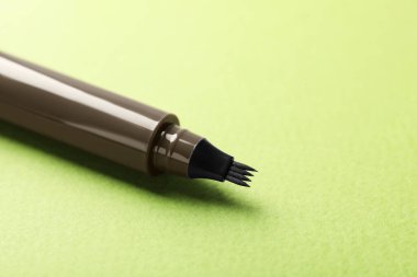 Yeşil arka planda bir adet sıvı kaş kalemi, yakın plan. Metin için boşluk