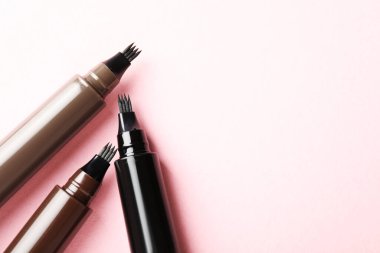 Açık pembe arka planda sıvı kaş kalemleri, düz yatış. Metin için boşluk