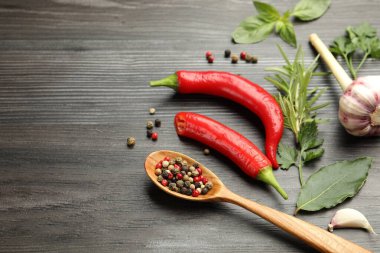 Farklı aromatik otlar, ürünler ve koyu ahşap masa üzerinde biberli kaşık, yakın plan. Metin için boşluk