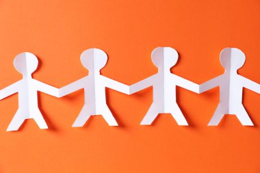 Turuncu arka planda el ele tutuşan insanların kağıt figürleri.