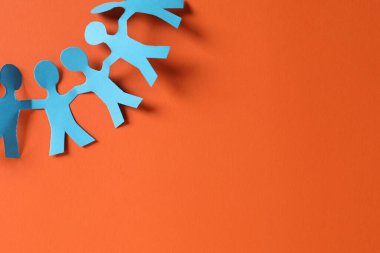 Turuncu arka planda el ele tutuşan insanların kağıt figürleri. Metin için boşluk