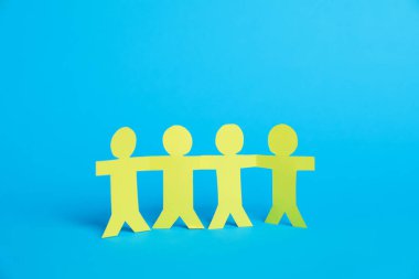 Açık mavi arka planda el ele tutuşan insan kağıt figürleri