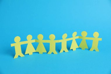 Açık mavi arka planda el ele tutuşan insan kağıt figürleri