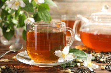 Aromatik yasemin çayı cam bardakta, çaydanlık, demlik ve çiçekler ahşap masada, yakın plan.